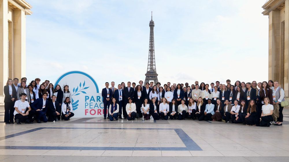 Volunteers’ family photo at Palais de Chaillot with Paris Peace Forum’s Logo and the Eiffel Tower in the background.