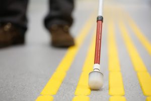 Blind pedestrian walking and detecting markings on tactile paving with textured ground surface indicators for blind and visually impaired. Blindness aid, visual impairment, independent life concept. De zlikovec. Shutterstock
