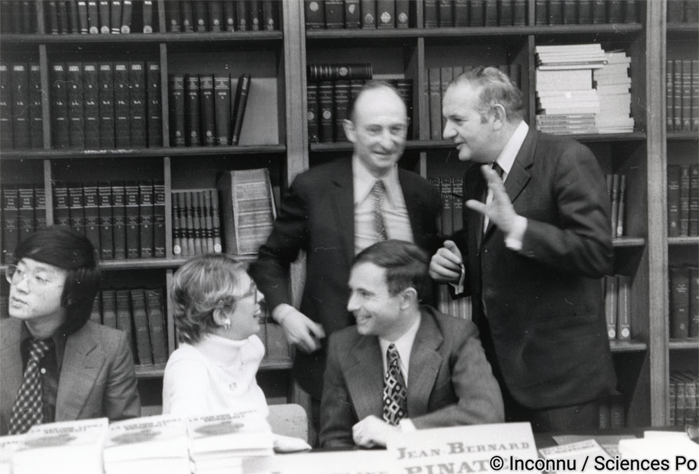Le 11 décembre 1976, à la bibliothèque, Alfred Grosser (debout à droite) en compagnie de Raymond Aron assiste à une séance de dédicace organisée par le bureau des étudiants pour la sortie du livre La guerre civile mondiale de Jacqueline Grapin et Jean-Bernard Pinatel (tous deux assis). Inconnu / Sciences Po