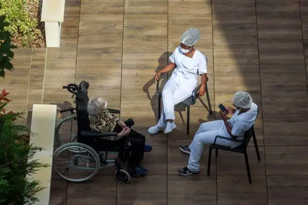 nurses caring for elderly or disabled people in a nursing home during the coronavirus pandemic Covid-19. Carers having a break in th sun with an old woman resident.