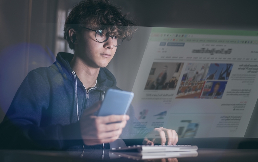 Adolescent reading newspaper on computer and smartphone