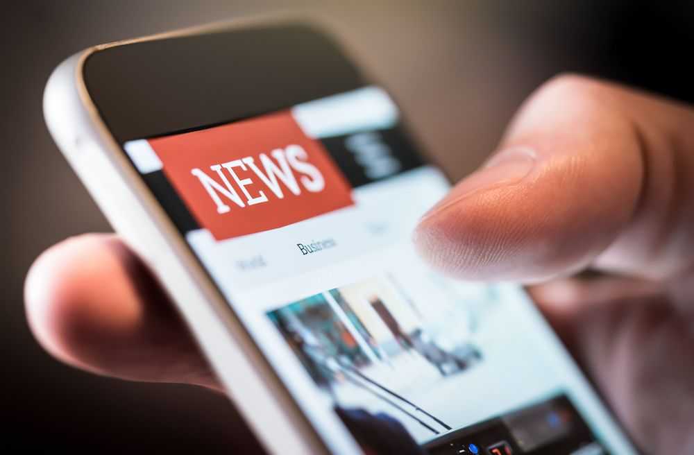 Online news on mobile phone. Close-up on a smartphone screen. Man reading articles in an app. Hand holding a smart device. Show the website. Online newspaper and portal.