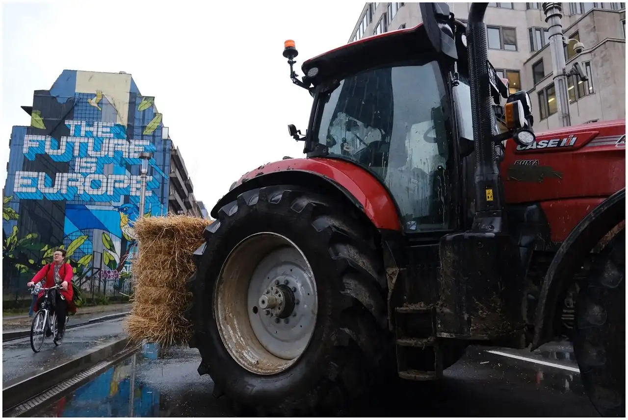 Un tracteur au premier plan, devant une peinture murale "The futur is Europe", au coeur de Bruxelles. Un cycliste passe.