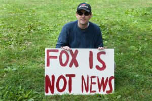 Boston, MA/USA- September 7, 2009: A participant in a Labor Day protest in the Boston Common supporting national healthcare reform sits on the grass holding a sign reading "FOX IS NOT NEWS." Crédits : Right Coast Images, Shutterstock 