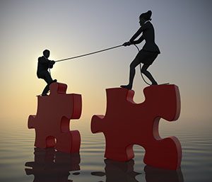 Team pulling giant jigsaw puzzle into position at sea at sunrise. Two executives pull giant jigsaw puzzle pieces into position at sunrise demonstrating teamwork at sea. Crédits : emerge, Shutterstock