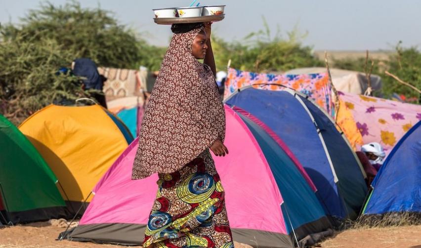 September 2013: woman in traditional clothing carry food in tent camp in Sahel z